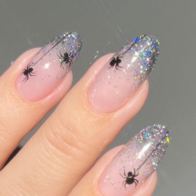 Delicate-oval-glitter-spider-nails-featuring-sheer-nude-pink-polish,-sparkling-silver-holographic-tips,-and-tiny-black-dangling-spiders.