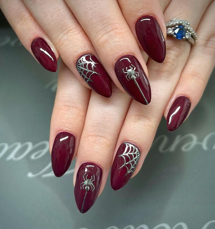 Glossy-burgundy-simple-spider-nails-on-almond-shapes,-featuring-delicate-metallic-silver-spiderweb-linework-and-hanging-spiders.