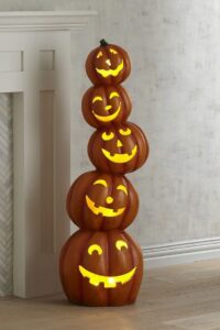 stacked-glowing-jack-o-lantern-pumpkin-tower-standing-next-to-a-white-fireplace