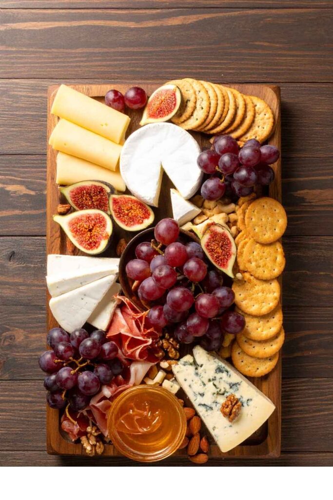 charcuterie-board-with-assorted-cheeses-crackers-red-grapes-sliced-figs-and-honey
