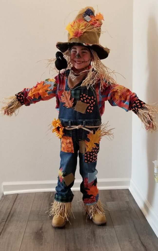child-wearing-a-diy-scarecrow-costume-with-patched-overalls-straw-accents-a-straw-hat-and-a-crow-on-their-shoulder