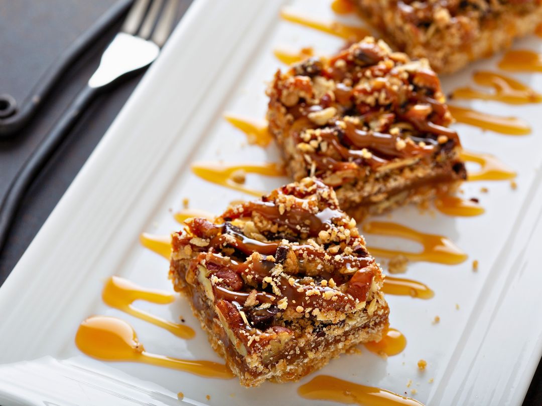 maple-pecan-bars-drizzled-with-caramel-sauce-on-a-white-serving-platter-with-a-fork
