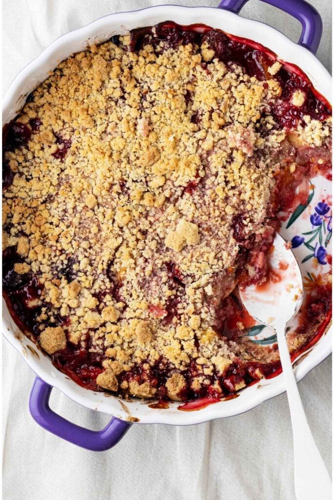 a-baked-fruit-crumble-in-a-purple-baking-dish-with-a-serving-spoon