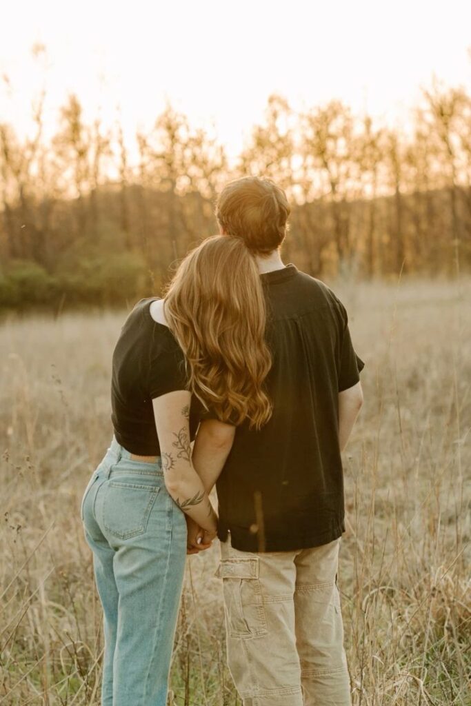 back-view-of-couple-cuddling-and-holding-hands-in-grassy-field