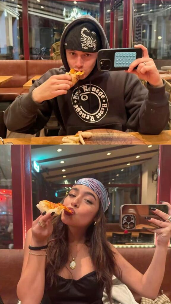 A-split-screen-showing-a-man-and-a-woman-eating-pizza-while-taking-mirror-selfies-on-a-virtual-dinner-date-for-Valentines-Day-gift-ideas 