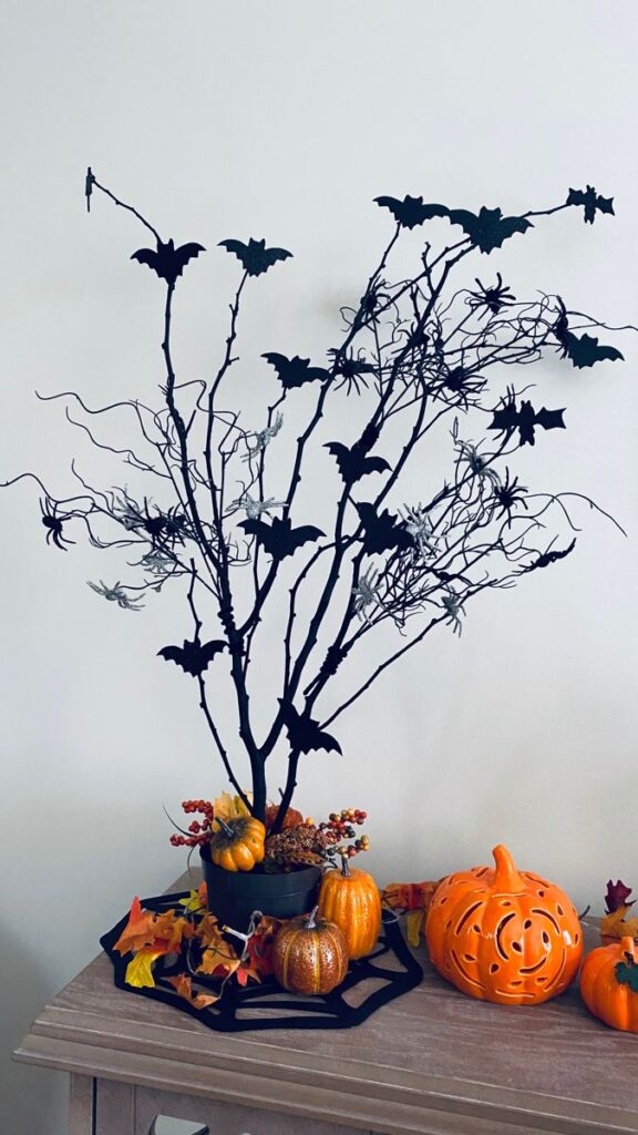 black-halloween-tree-branch-centerpiece-adorned-with-cutout-bats-surrounded-by-ceramic-and-glittered-pumpkins