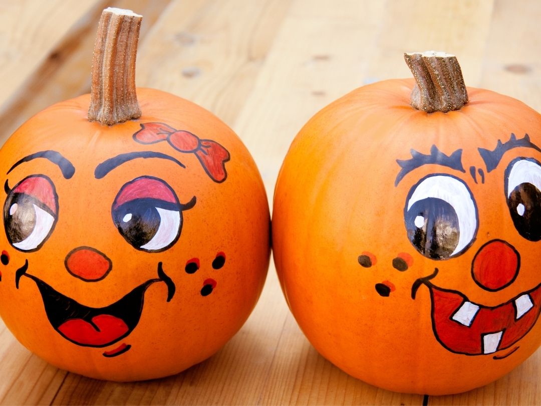 two-orange-pumpkins-painted-with-playful-cartoon-faces-and-expressions-sitting-on-a-wooden-surface-for-Halloween-Decor-Ideas