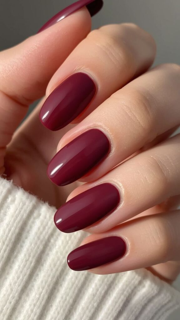 deep-burgundy-glossy-oval-nails-with-white-knit-sweater-sleeve-fall-nail-designs