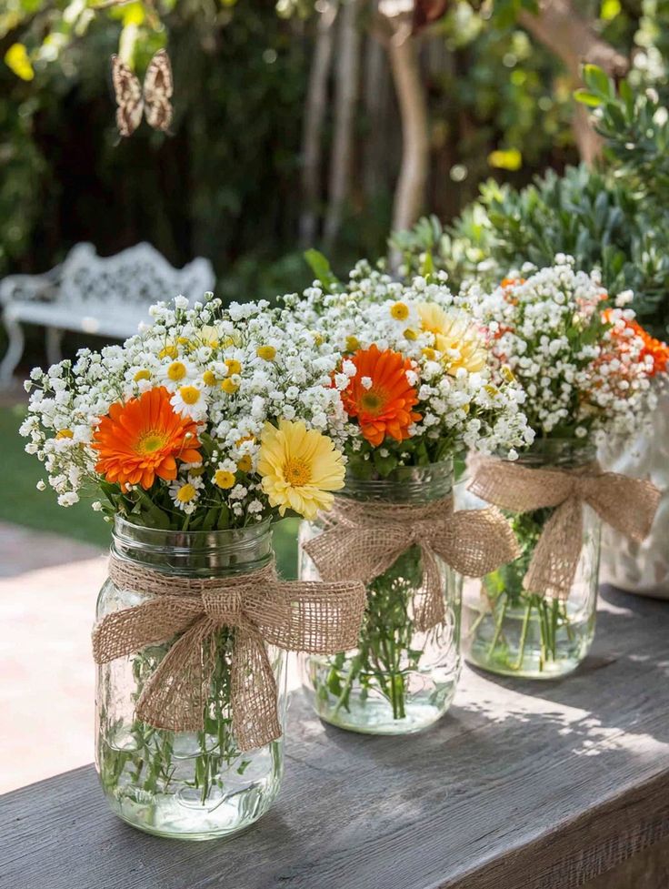 three-mason-jars-with-burlap-bows-holding-white-yellow-and-orange-flowers
