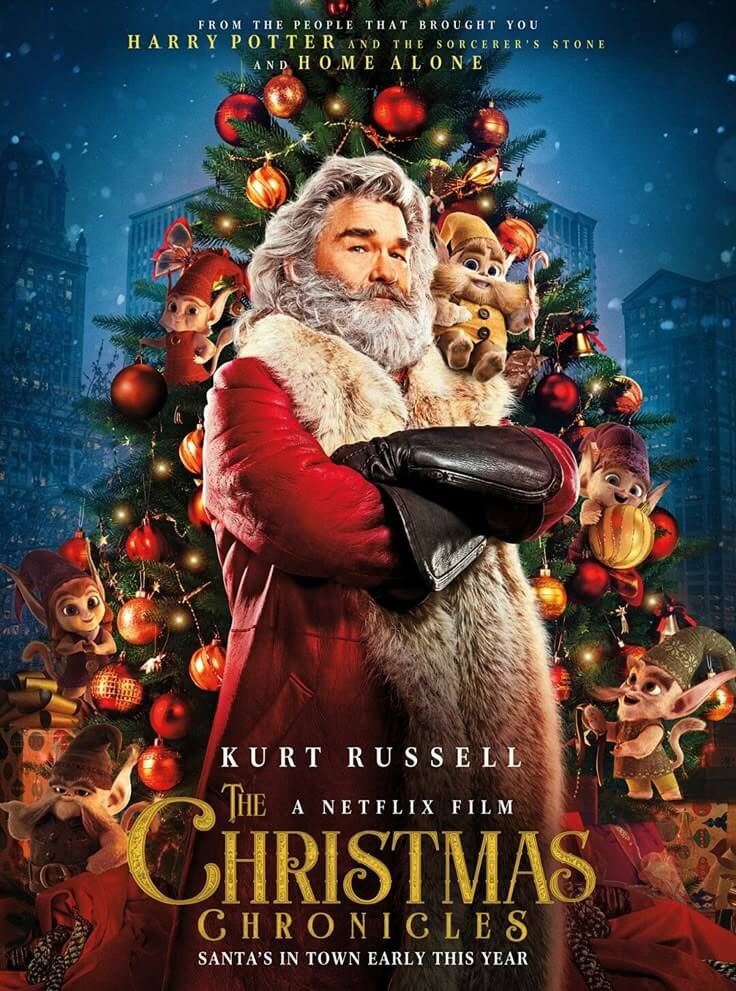 `movie-poster-for-the-christmas-chronicles-starring-kurt-russell-as-santa-claus-with-his-arms-crossed-in-front-of-a-decorated-christmas-tree-surrounded-by-tiny-elves`
