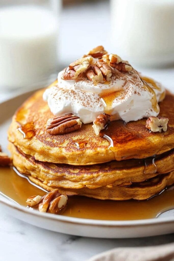 fluffy-pumpkin-pancakes-stacked-with-whipped-cream-chopped-pecans-cinnamon-and-maple-syrup