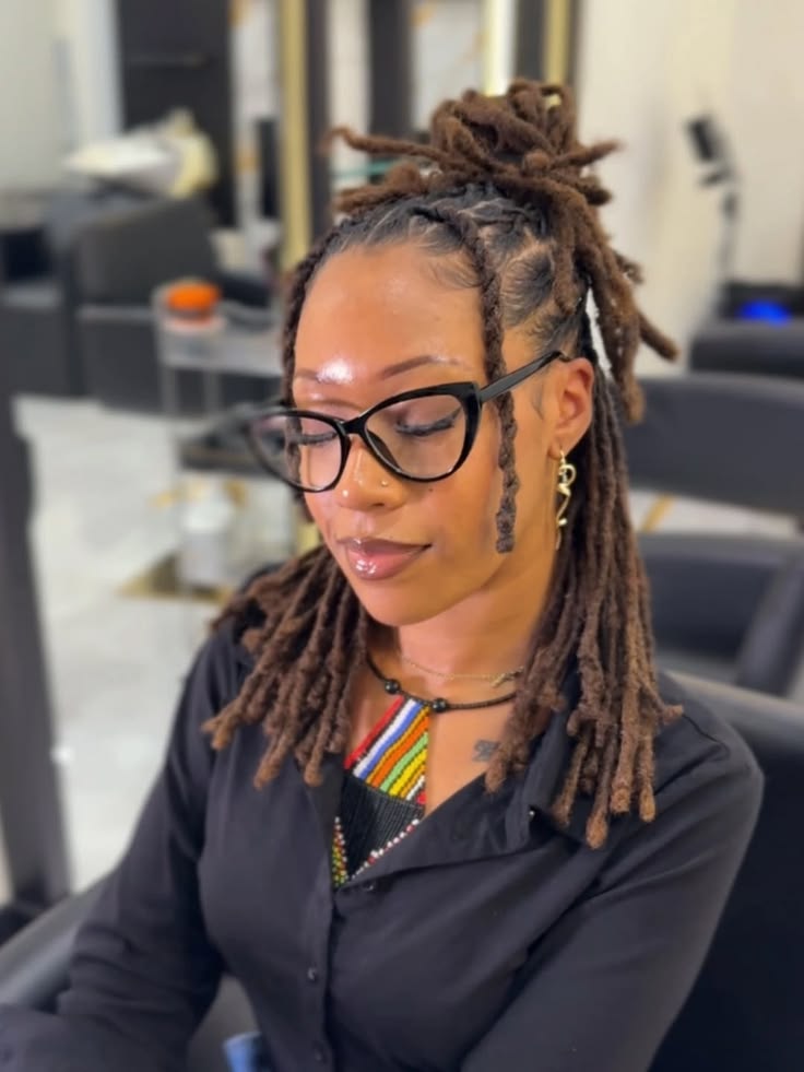 Woman with medium length locs styled in a half-up ponytail wearing black glasses and a colorful beaded necklace